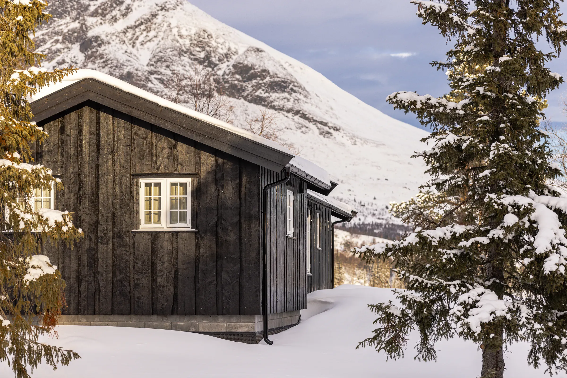 Cabin at Lykkja with black cladding and snow-covered mountains behind
